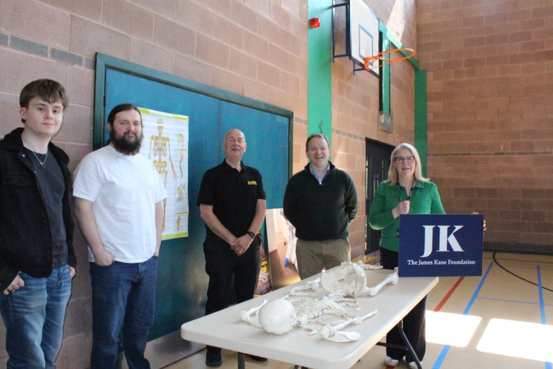 Students and staff at SERC Bangor Campus with a model human skeleton and a James Kane Foundation logo on a signboard